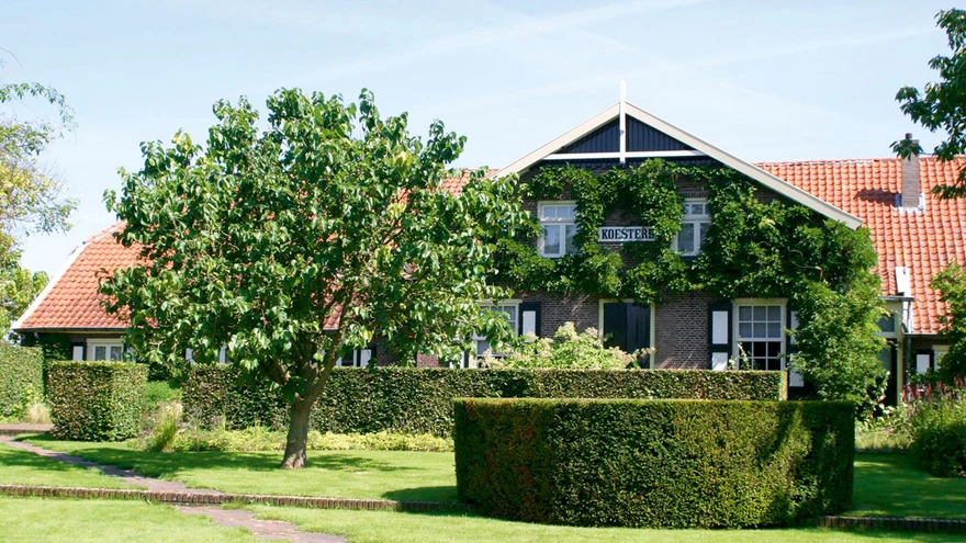  Piet Oudolfi elumaja ja vaade eesaia algusesse. Üle muru viiv diagonaalne sillutatud teerada näitab külastajatele teed näidisaiani. Pildil paistev madal silindrikujuline jugapuudest vorm on aiadisaineri varasema loomingu meenutus. 